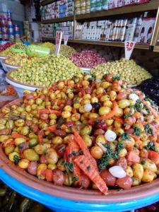 Olives piled high in a conical shape at a market with so many varieties of olives.
